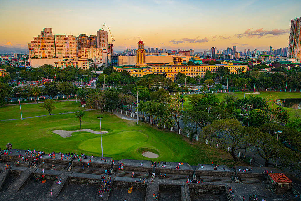 Panoramic view of Intramuros city walls at golden hour with historic clock tower and Manila skyline — best things to do in Manila