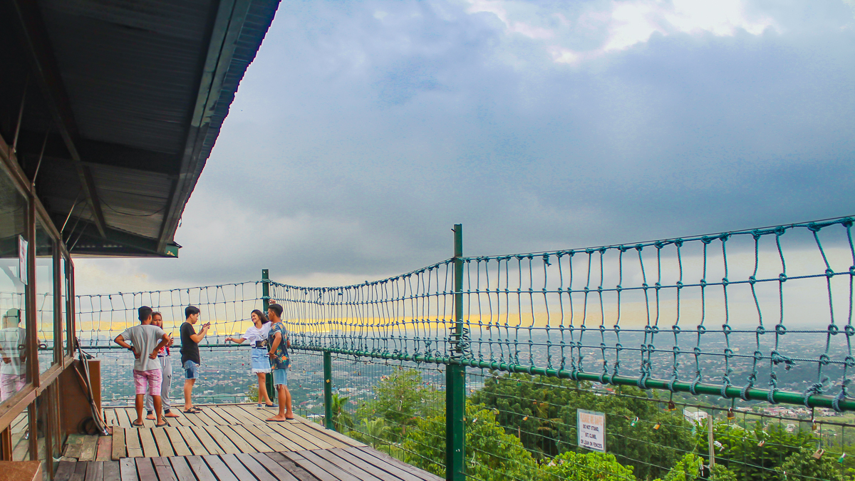 Visitors standing beside the Cloud 9 Antipolo hanging bridge and view deck overlooking the Rizal landscape during sunset