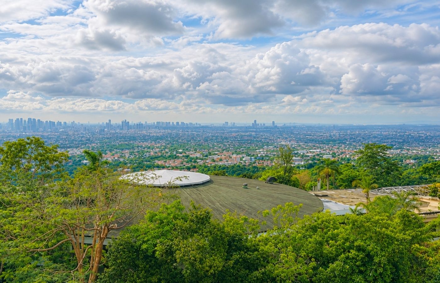 Panoramic view from Cloud 9 Antipolo overlooking Metro Manila skyline beneath dramatic clouds and lush hillside greenery.