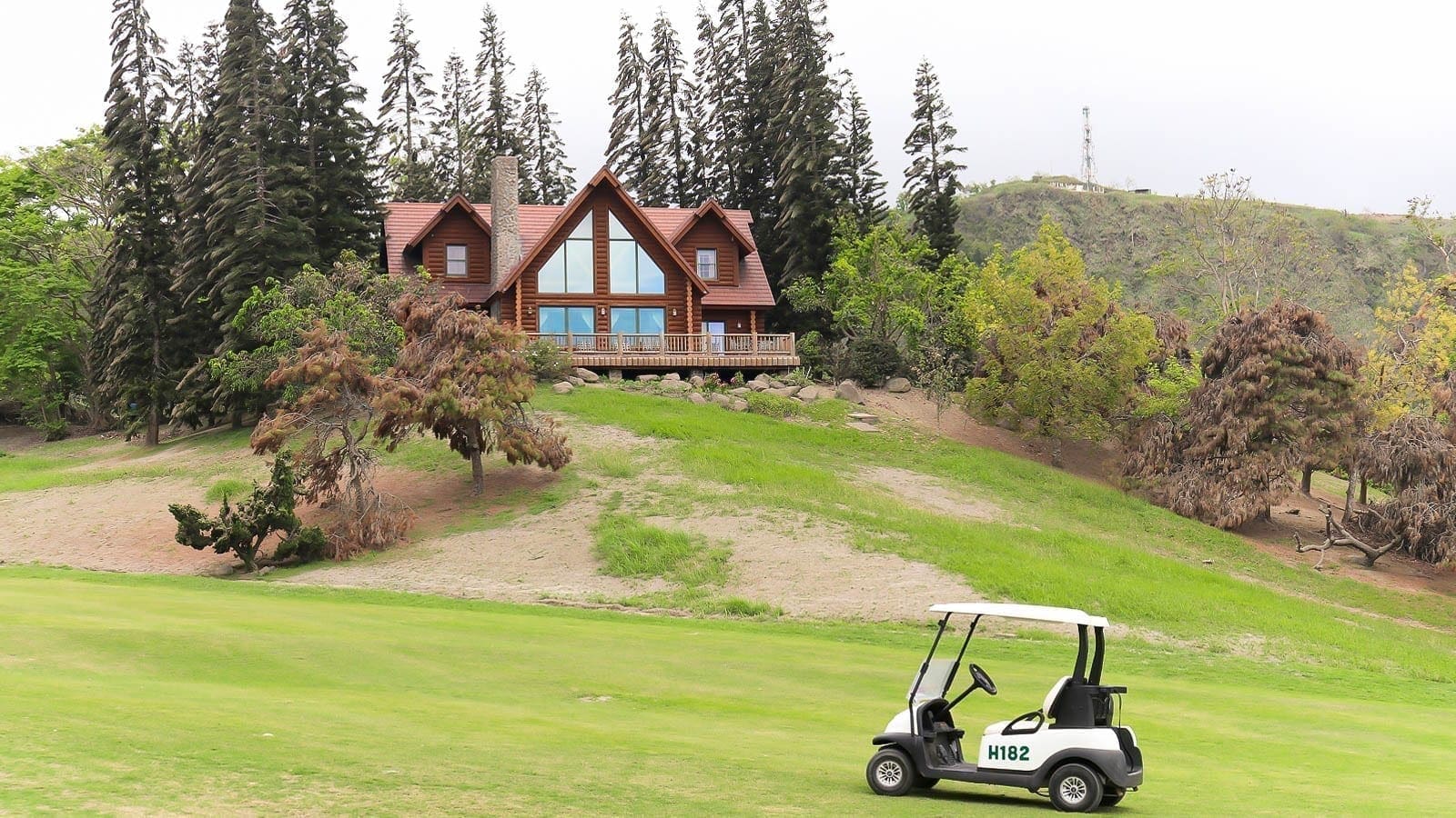 Golf cart passing a mountain cabin in Tagaytay Highlands surrounded by pine trees