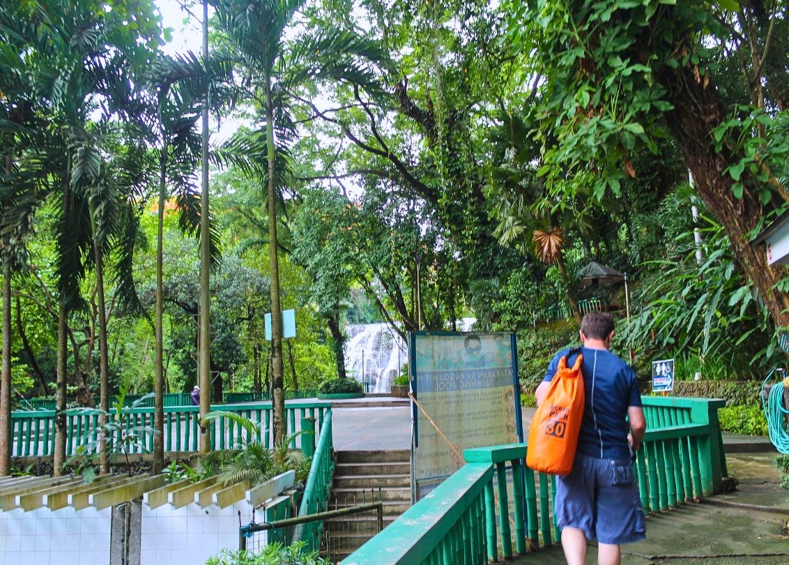 Visitor with an orange backpack walking toward Hinulugang Taktak Falls past the park’s concrete paths and picnic areas
