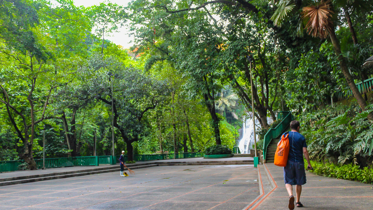 Visitor walking toward Hinulugang Taktak Falls along a shaded concrete path, Antipolo, Rizal