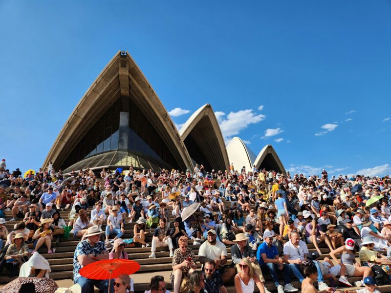 Moving to Australia — diverse crowd gathered at the Sydney Opera House forecourt on a sunny day