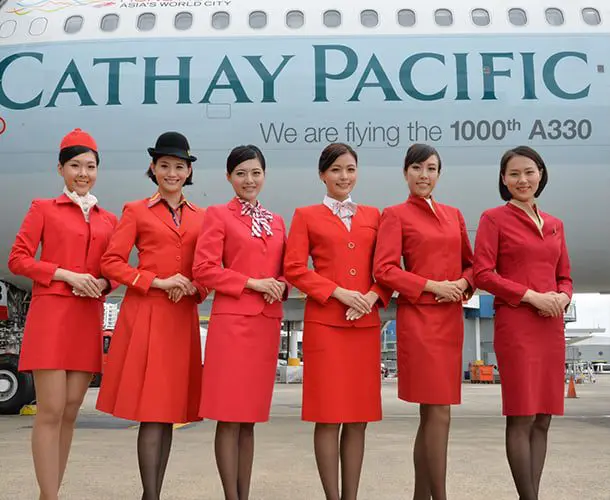 Hot air hostess Cathay Pacific cabin crew in red uniform standing in front of aircraft, showing polished presentation and controlled elegance in airline branding
