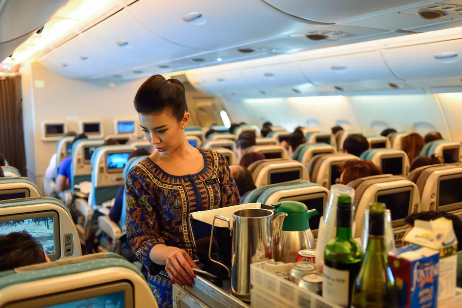 Flight attendant serving passengers in economy cabin showing controlled service behavior and emotional labor