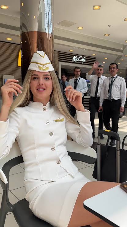Flight attendant in white uniform standing in airport terminal with cabin crew in background