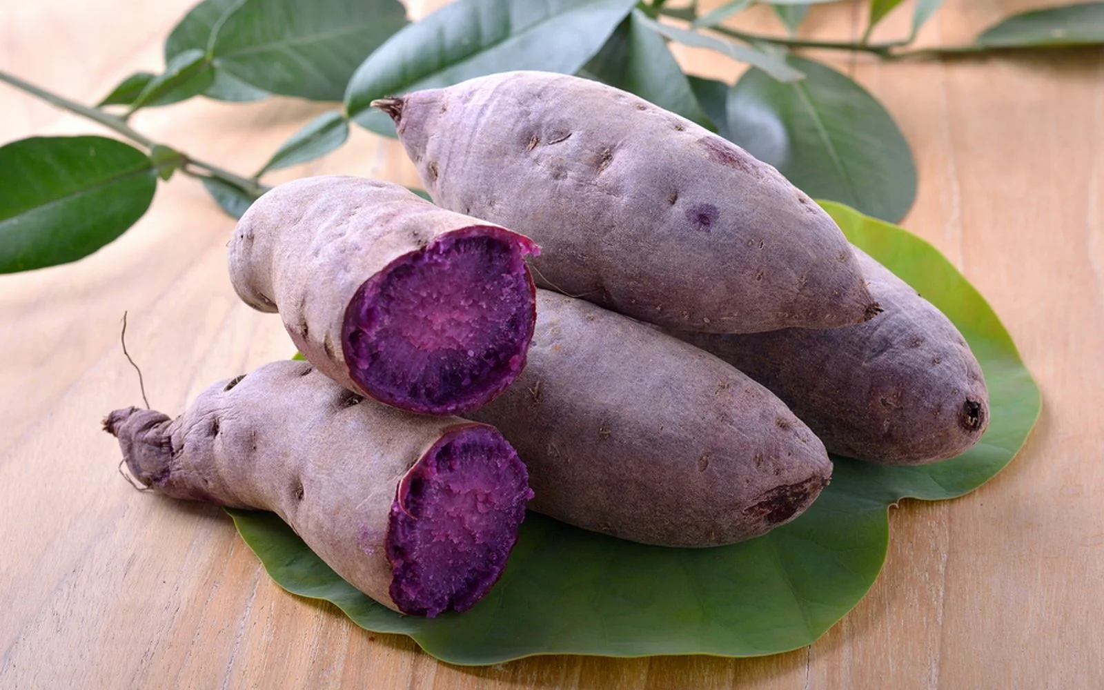 Fresh ube tubers on a leaf with one cut open showing deep purple flesh from the Philippines