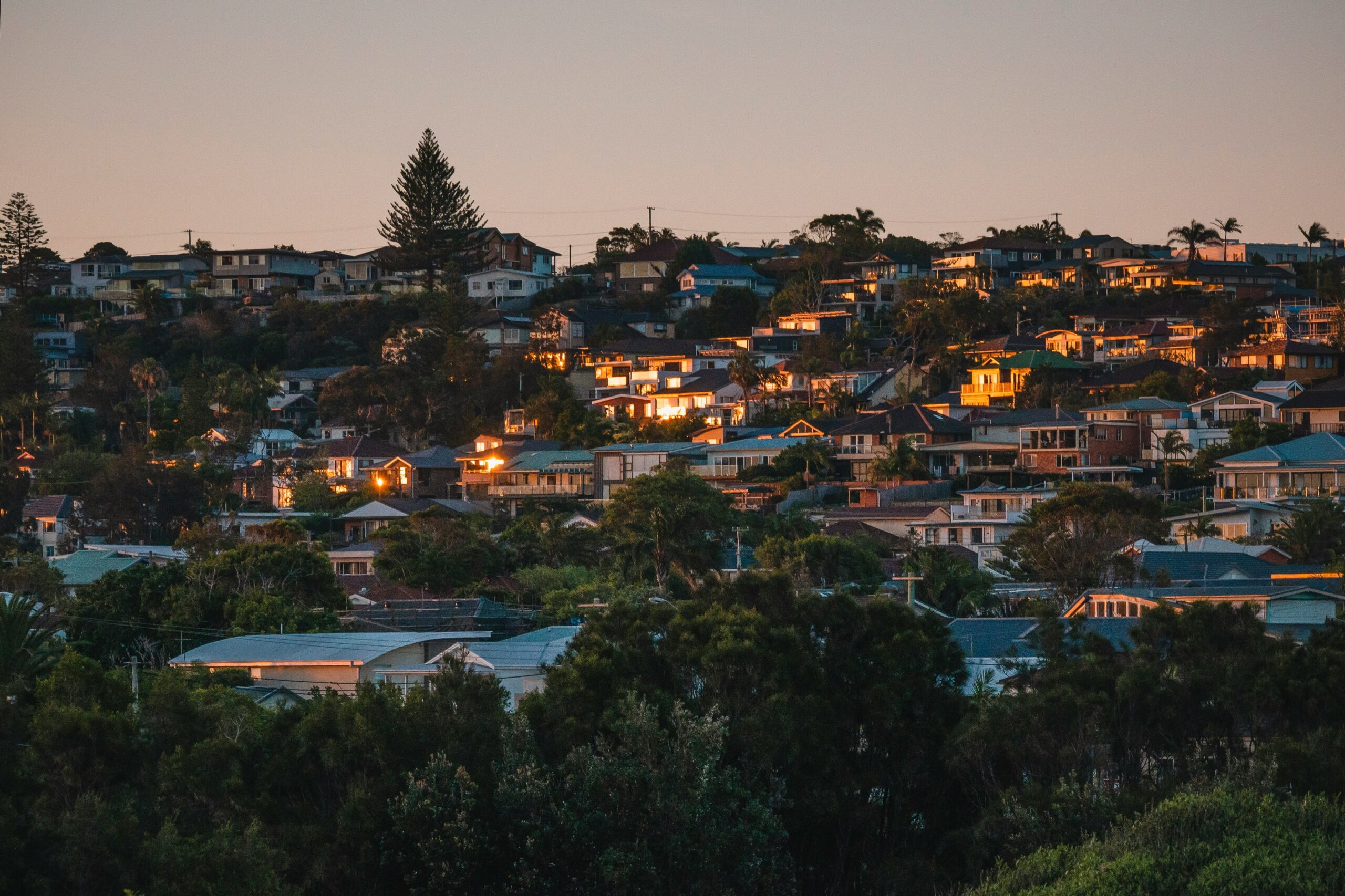 Aerial night view of Sydney's densely packed urban landscape with illuminated buildings, representing the high cost of living in Australia for migrants facing some of the highest median weekly rents in the country.