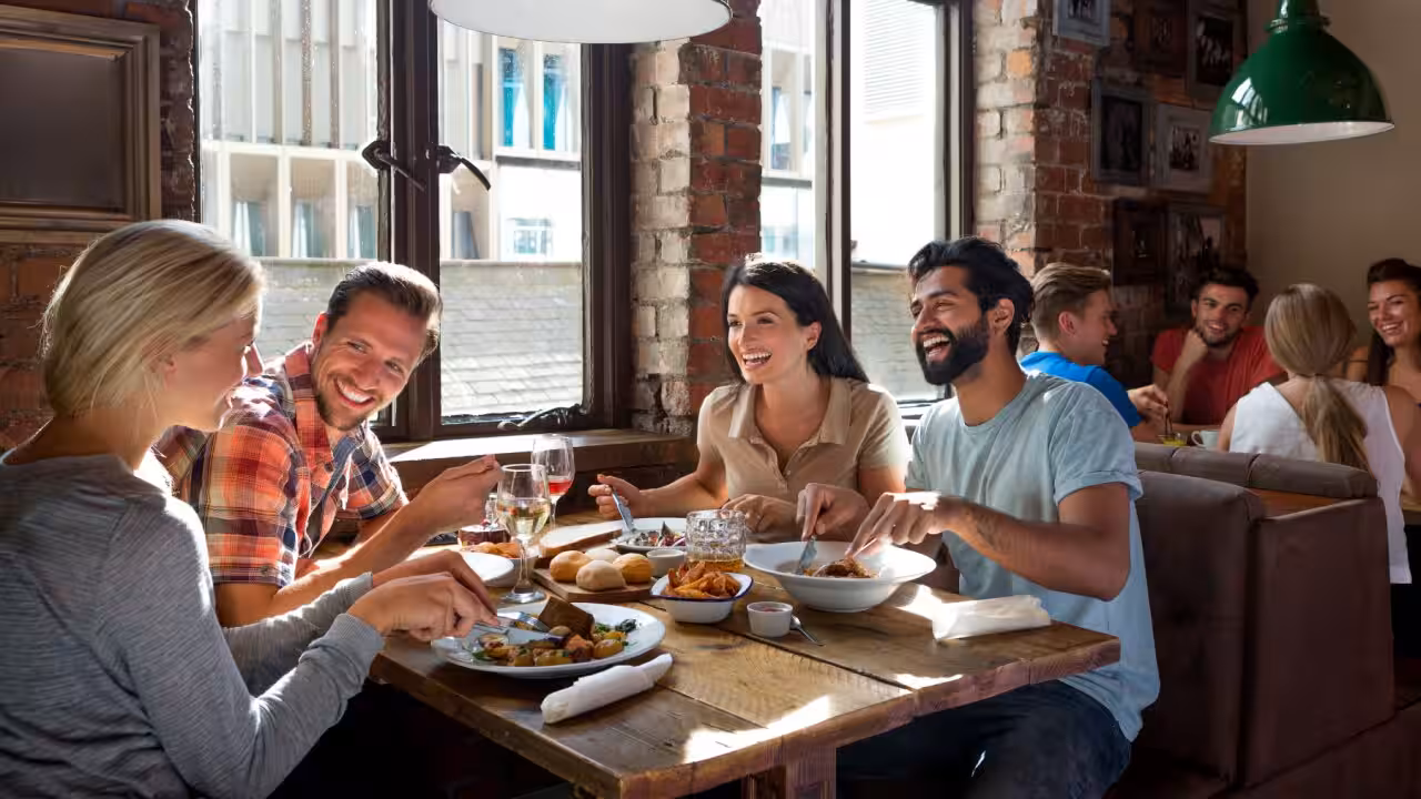 Friends laughing together during dinner, showing how Australian humour and tall poppy syndrome use teasing as a sign of social acceptance.